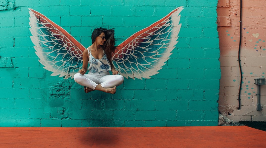 Γυναίκα που αιωρείται σε στάση οκλαδόν με φόντο γκράφιτι που δείχνει φτερά