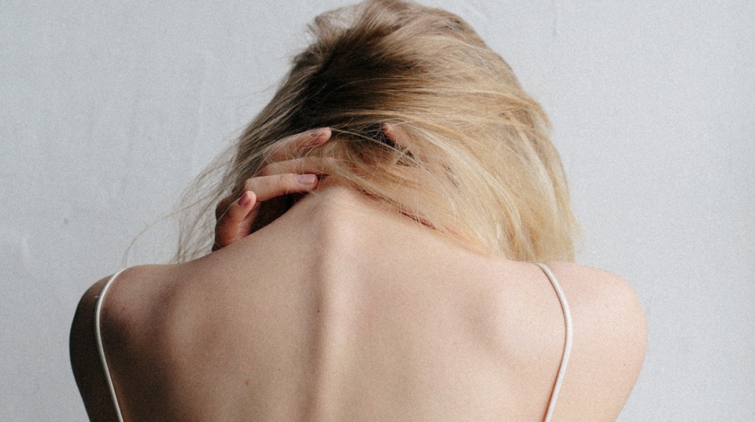 Γυναίκα με γυρισμένη πλάτη και σκυμμένο κεφάλι, κρατάει τον αυχένα της