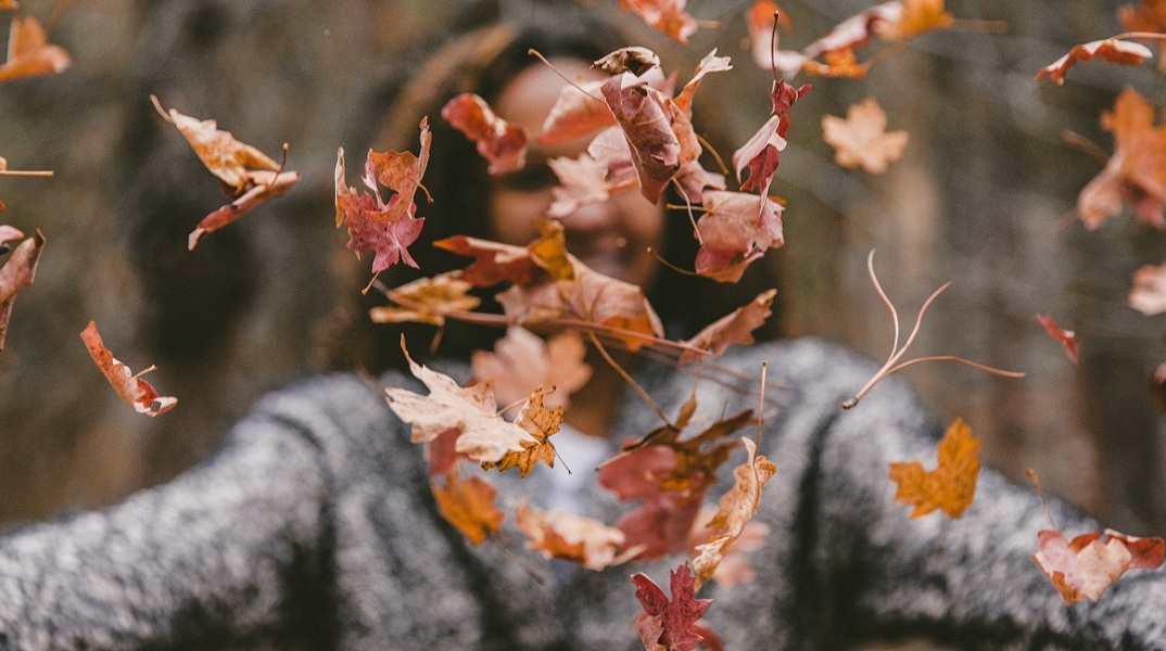 Ένα κορίτσι πετάει στον αέρα φθινοπωρινά φύλλα.