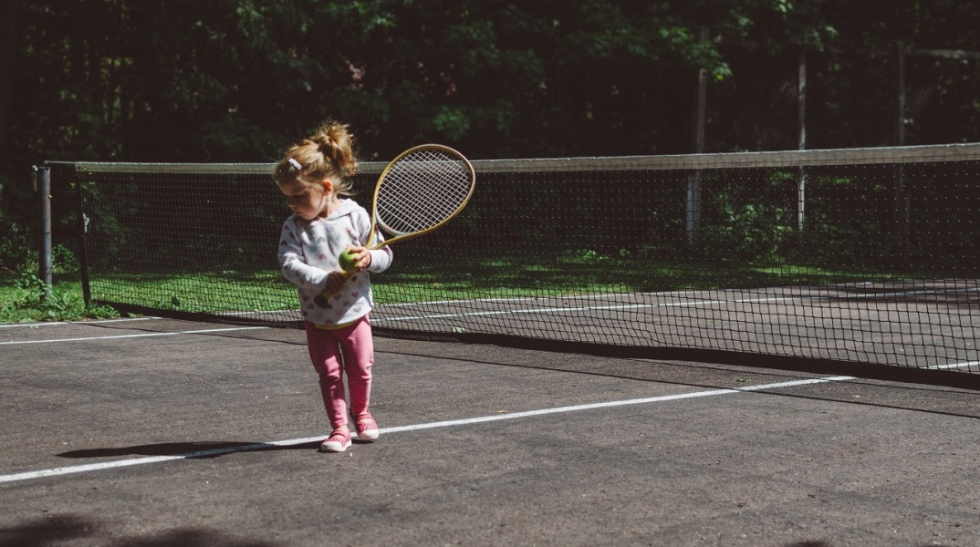 Μικρό κορίτσι σε γήπεδο τένις με μπαλάκι και ρακέτα τένις