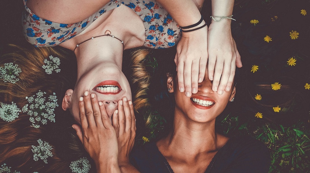Δύο γυναίκες χαμογελάνε ενώ κλείνουν τα μάτια η μια στην άλλη 