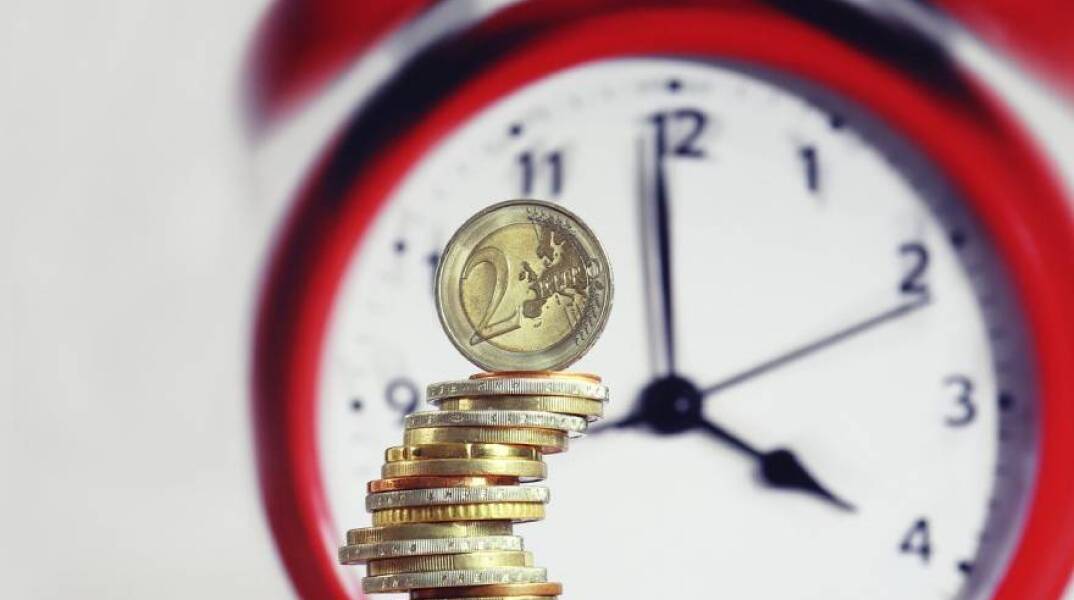 Νομίσματα ευρώ μπροστά από ρολόι