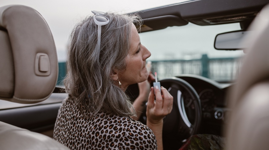 Γκριζομάλλα γυναίκα σε αυτοκίνητο βάζει κραγιόν στον καθρέφτη