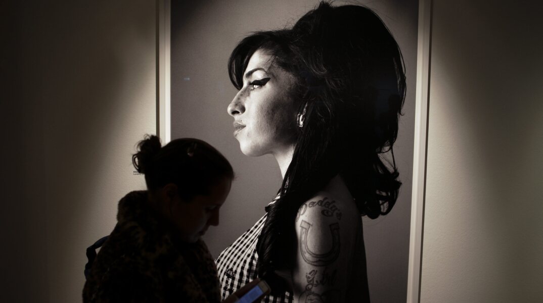 Γυναίκα κοιτά το smartphone της με φόντο πορτρέτο της Amy Winehouse