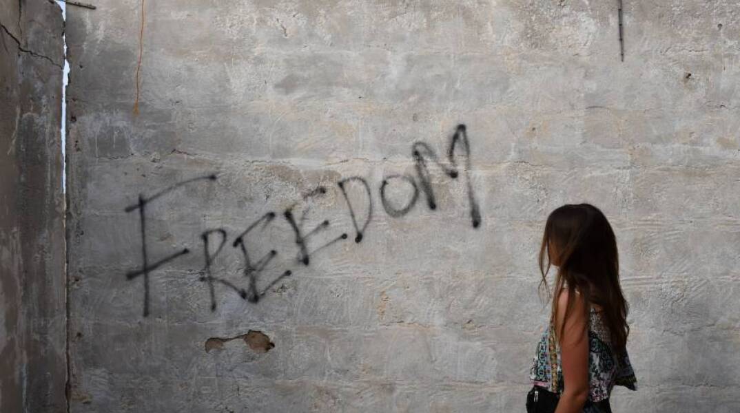 Γυναίκα κοιτάει έναν τοίχο όπου είναι γραμμένη η λέξη Freedom (Ελευθερία)