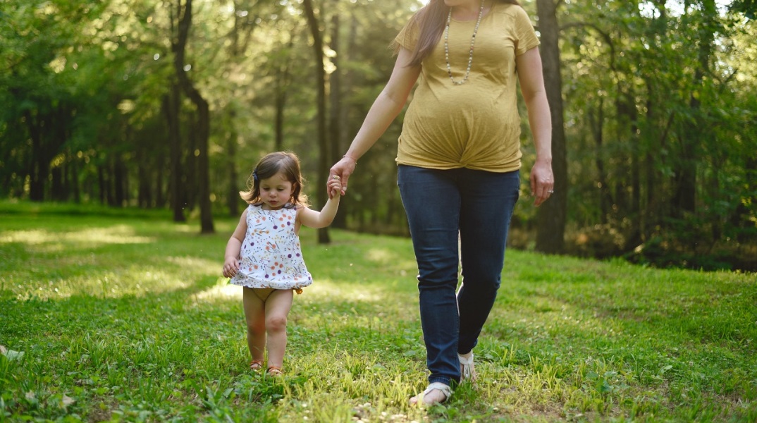 Έγκυος γυναίκα κρατάει από το χέρι μικρό κοριτσάκι σε δάσος
