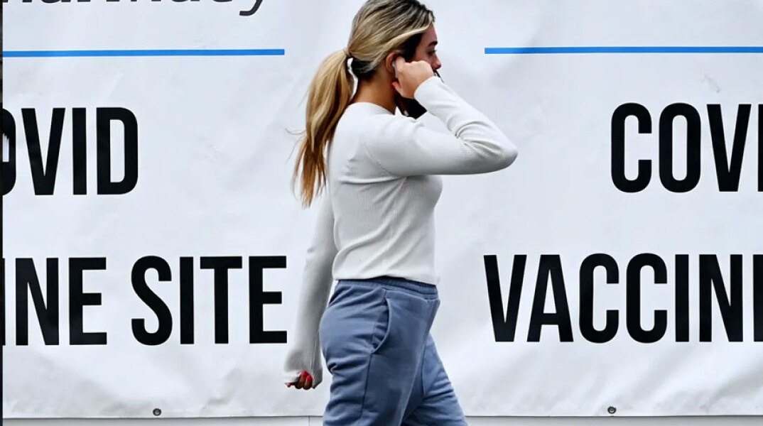 Κοπέλα στις ΗΠΑ μιλά στο κινητό, περνώντας μπροστά από αφίσες για τον εμβολιασμό κατά του κορωνοϊού