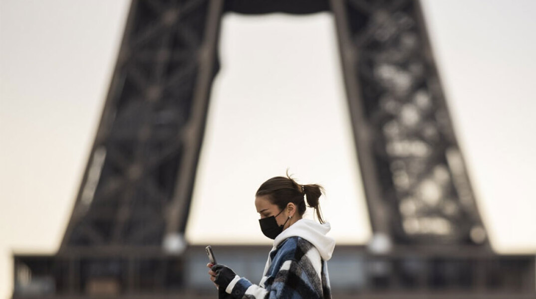 Κοπέλα με μάσκα για τον κορωνοϊό περνά μπροστά από τον Πύργο του Άιφελ στο Παρίσι