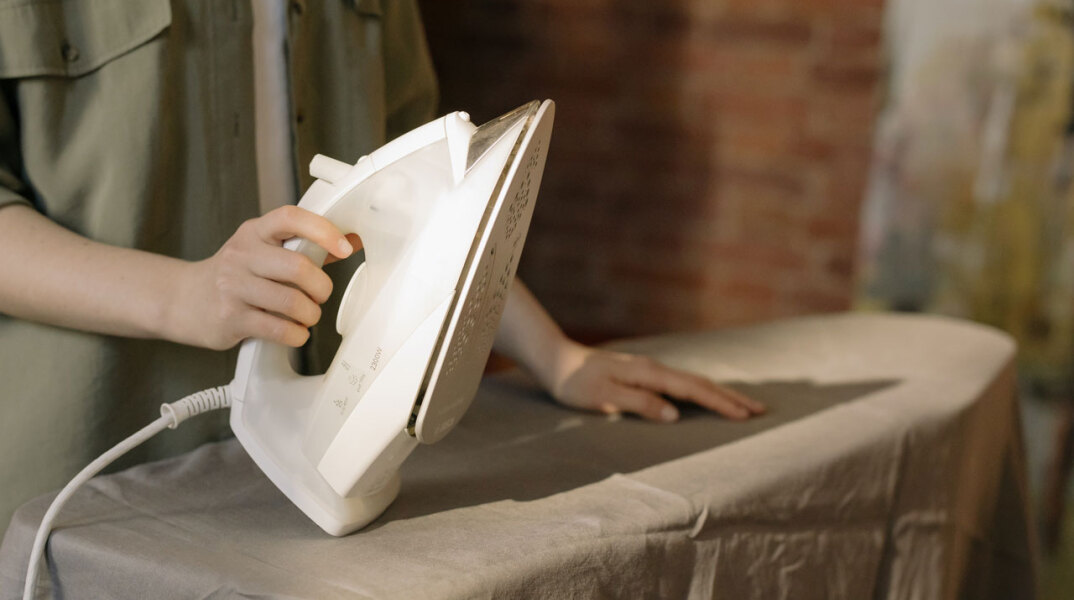 Γυναίκα κρατάει σίδερο μπροστά σε σιδερώστρα