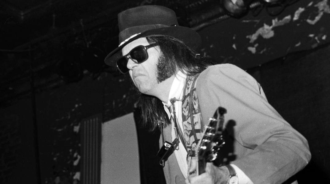O Neil Young παίζει κιθάρα και φορά μαύρα γυαλιά