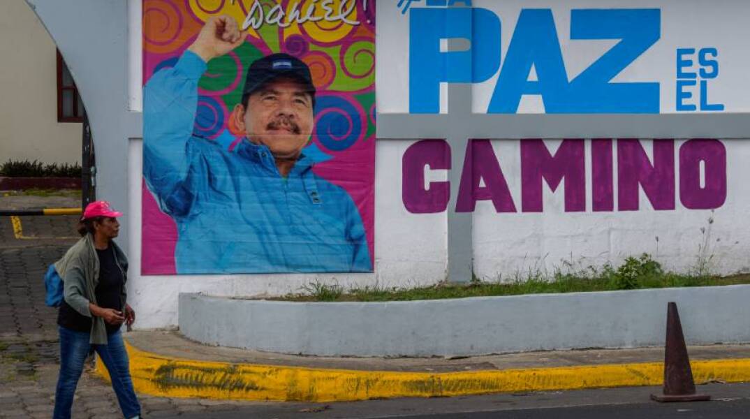Μια γυναίκα περπατά μπροστά από διαφημιστική αφίσα με την εικόνα του Προέδρου της Νικαράγουας, Ντάνιελ Ορτέγκα