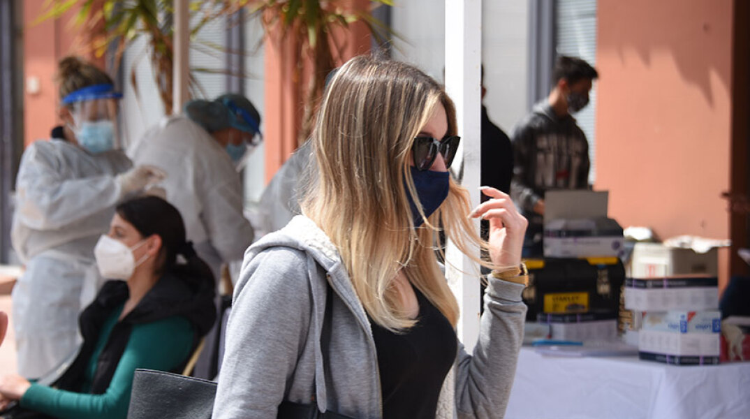 Κοπέλα με μάσκα περνά μπροστά από κινητό κλιμάκιο του ΕΟΔΥ που διενεργεί δωρεάν rapid test για κορωνοϊό