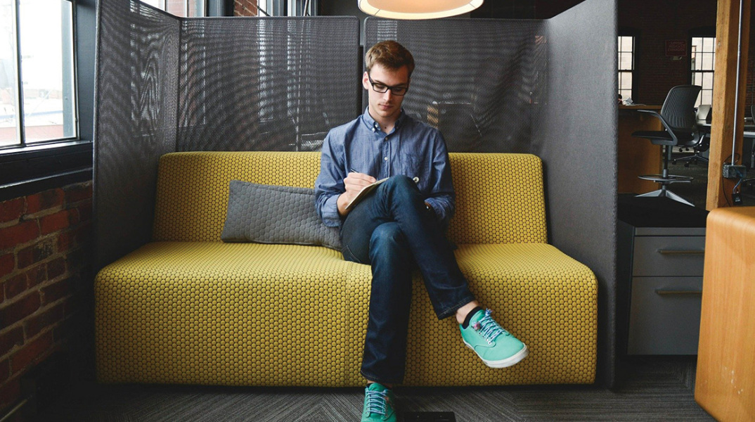 Νεαρός άντρας στον καναπέ εταιρείας, κρατάει σημειώσεις