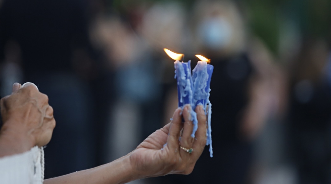 Γυναικείο χέρι που κρατά δύο αναμμένα κεριά σε εξωτερικό χώρο