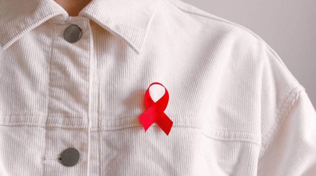 Άντρας με λευκό κοτλέ πουκάμισο και την κόκκινη κορδέλα κατά του HIV/AIDS