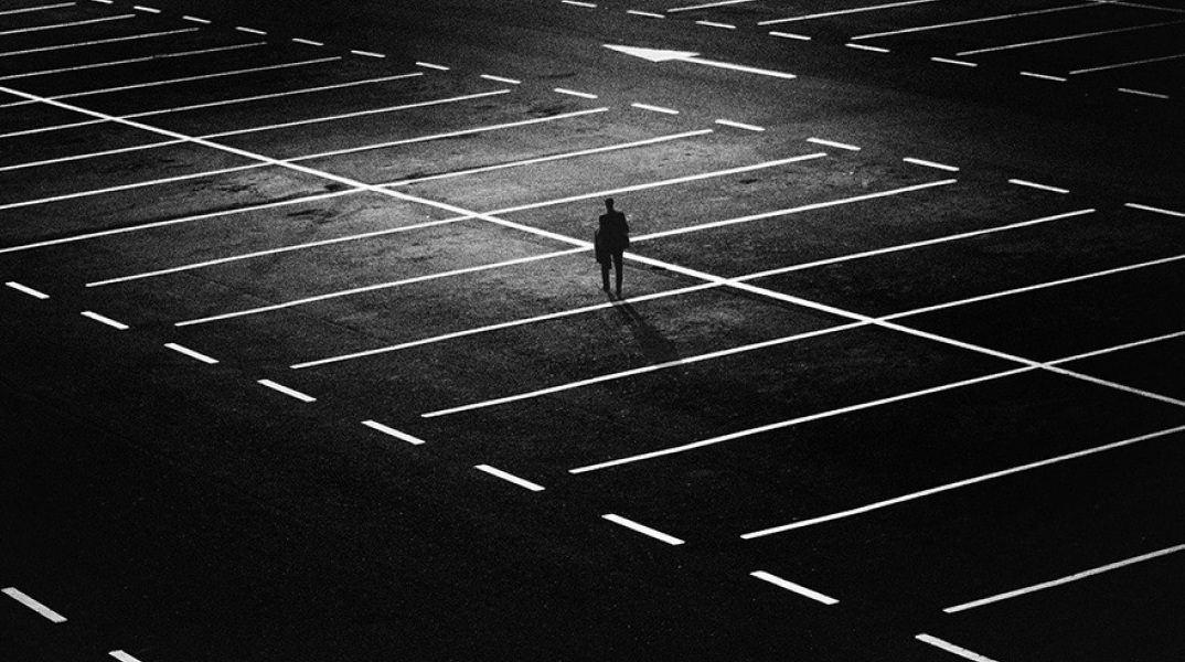 Ένας άντρας στέκεται στη μέση ενός άδειου πάρκινγκ τη νύχτα