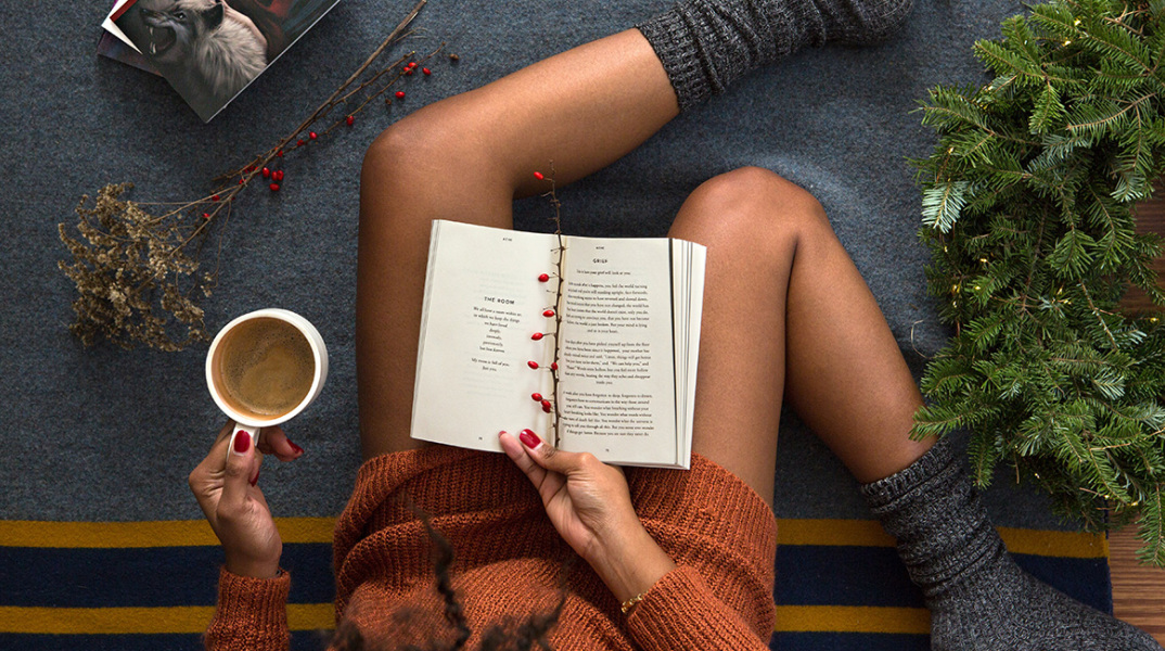 Μια κοπέλα καθισμένη με καφέ στο χέρι κι ένα βιβλίο στα πόδια της