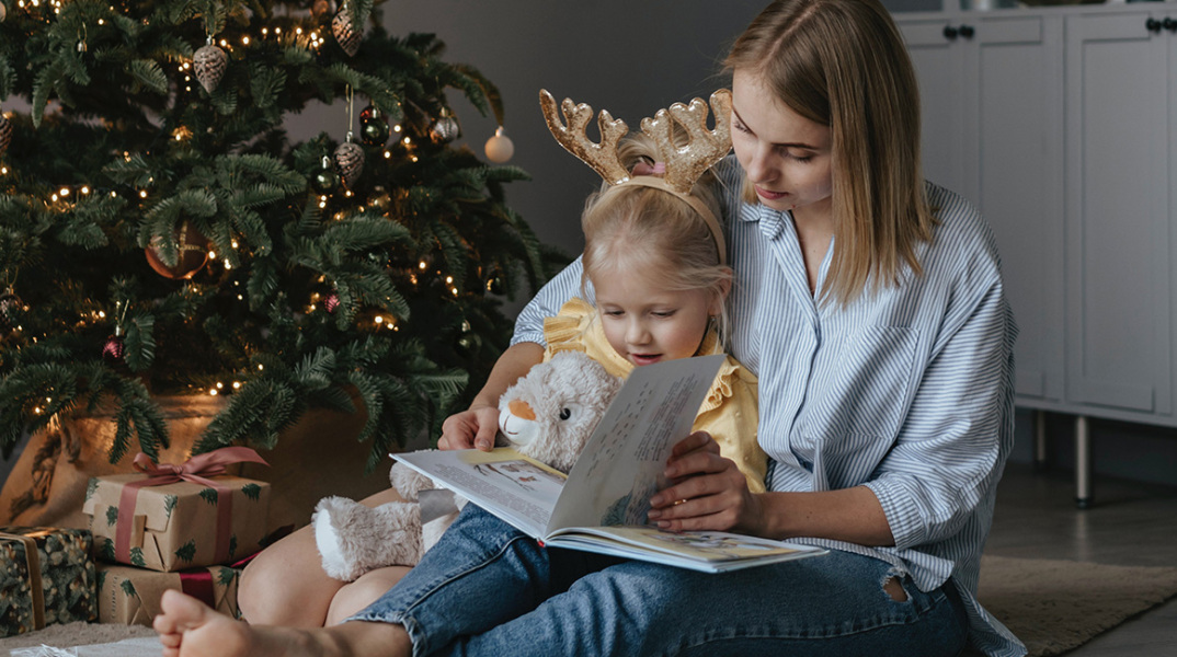 Μαμά και παιδί διαβάζουν βιβλίο δίπλα από το χριστουγεννιάτικο δέντρο