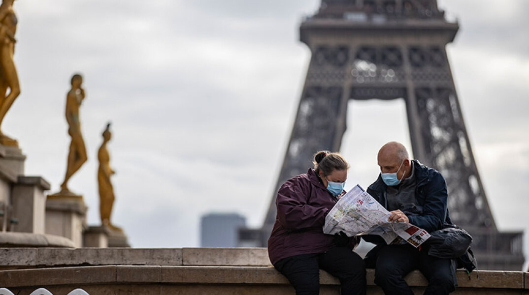 Πολίτες στη Γαλλία με μάσκα για τον κορωνοϊό με φόντο τον Πύργο του Άιφελ