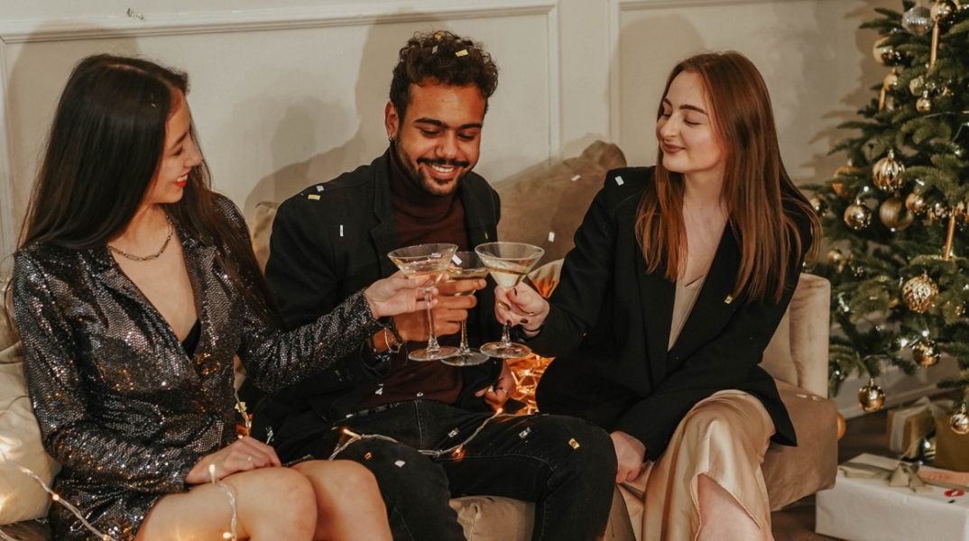 Τρεις φίλοι τσουγκρίζουν τα ποτά τους δίπλα από το χριστουγεννιάτικο δέντρο. 
