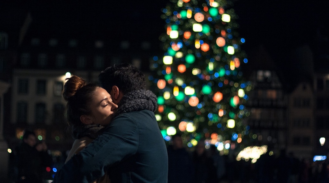 Ζευγάρι που αγκαλιάζεται με φόντο Χριστουγεννιάτικο δέντρο
