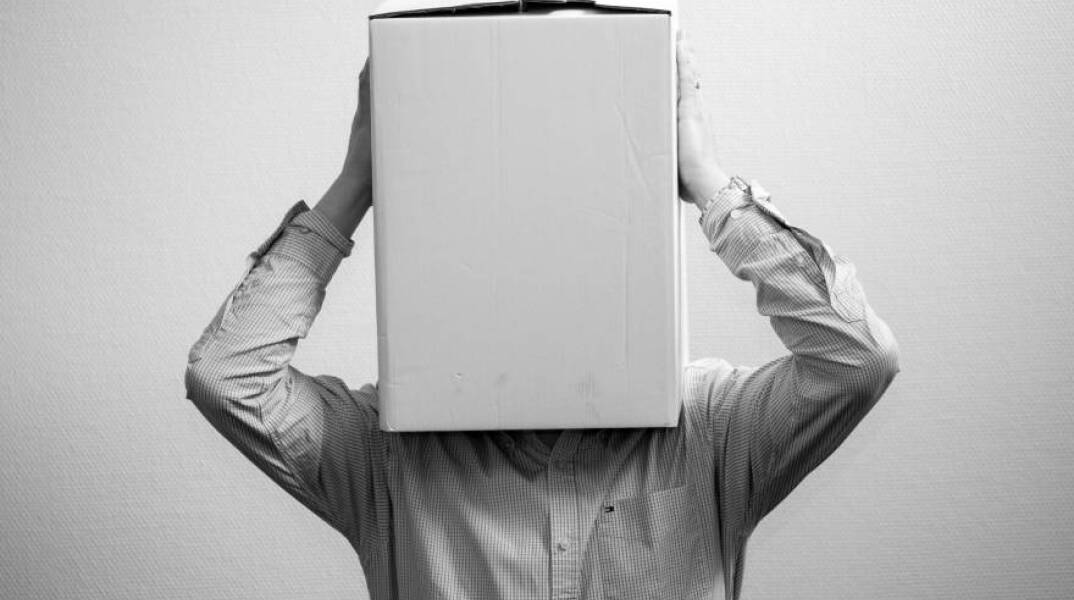 Ασπρόμαυρη φωτογραφία με έναν άντρα που έχει βάλει ένα κουτί στο κεφάλι του