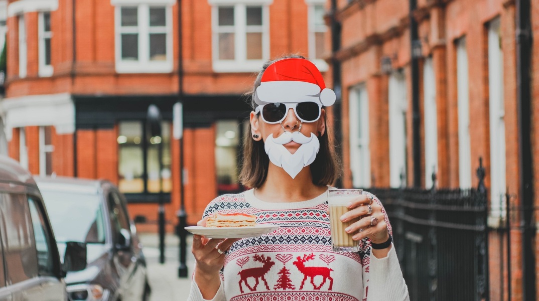 Γυναίκα με χριστουγεννιάτικη αμφίεση σε δρόμο που κρατά γλυκό και καφέ