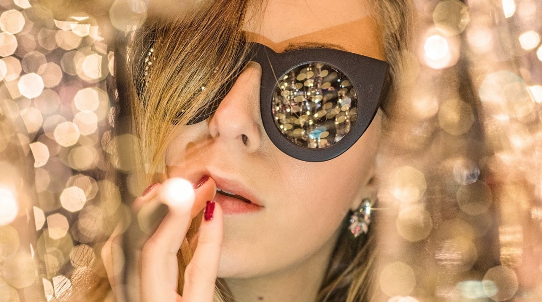 Γυναίκα με γυαλιά ηλίου ανάμεσα σε χρυσά χριστουγεννιάτικα λαμπάκια