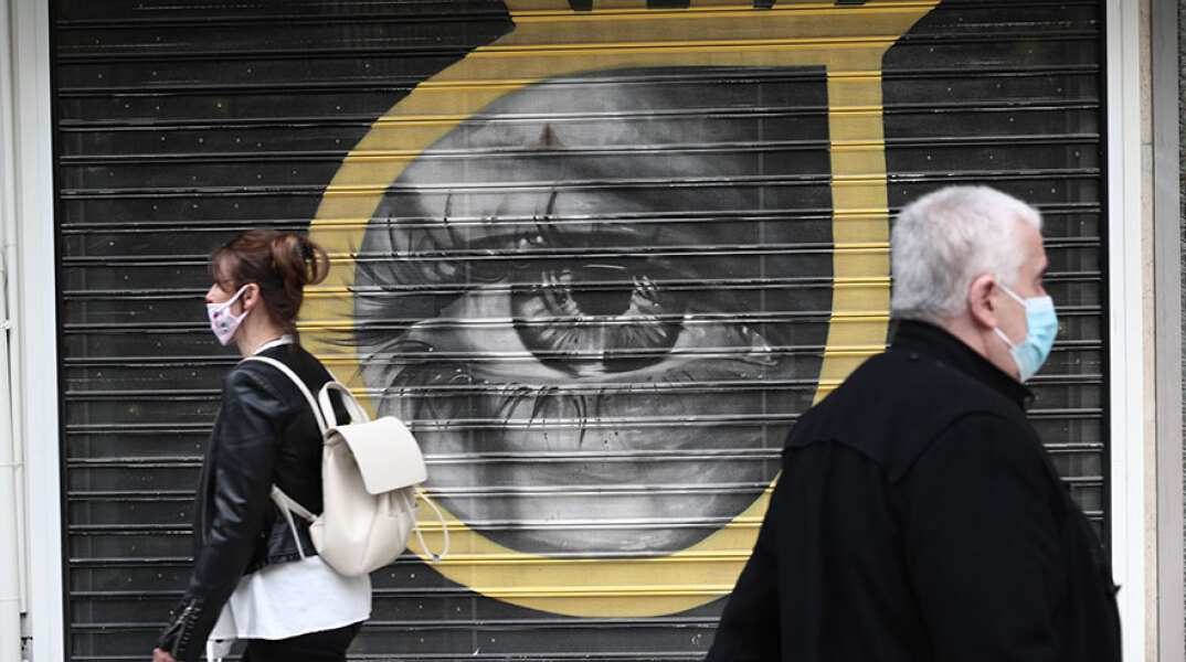 Πολίτες με μάσκα για κορωνοϊό μπροστά από γκράφιτι για την πανδημία Covid-19