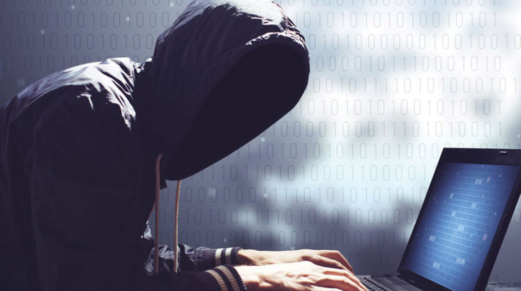 Άνθρωπος με κουκούλα και κρυμμένο πρόσωπο πληκτρολογεί σε υπολογιστή