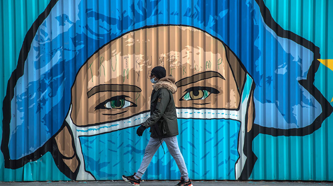Πολίτης με μάσκα για τον κορωνοϊό μπροστά από mural για την πανδημία Covid στο Παρίσι