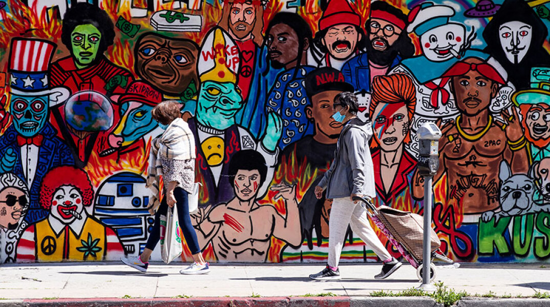 Πολίτες με μάσκα για κορωνοϊό στο Λος Άντζελες μπροστά από mural για το Χόλιγουντ