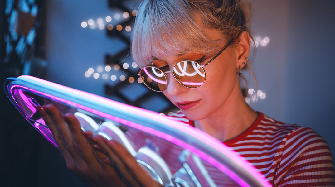 Κοπέλα με κοντά ηανθά μαλλιά κρατάει μια neon πινακίδα