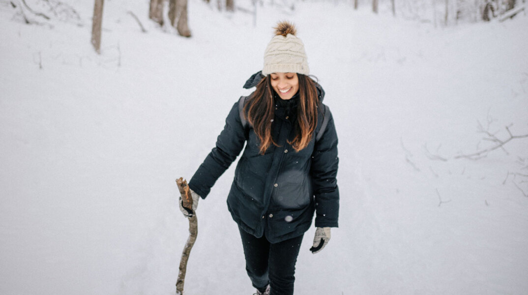 Κοπέλα με μαύρα ρούχα και λευκό σκουφάκι περπατάει στο χιόνι