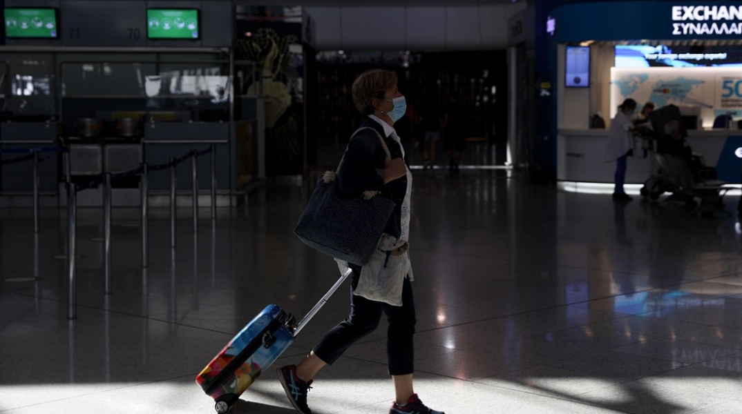 Γυναίκα με βαλίτσα φορά τη μάσκα κατά την παραμονή τους στους χώρους του αεροδρομίου