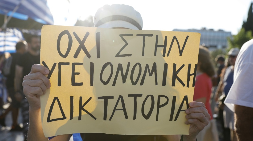 Γυναίκα που κρατά πλακάτ σε συγκέντρωση αντιεμβολιαστών