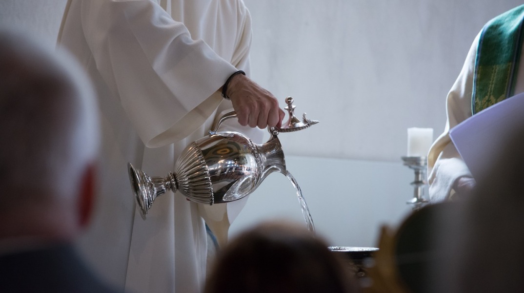 Ιερέας χύνει νερό στη κολυμβήθρα για την τέλεση της βάπτισης