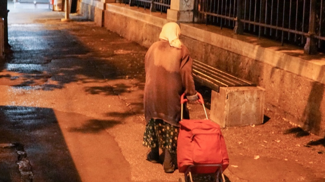 Ηλικιωμένη σέρνει το καρότσι της σε δρόμο 