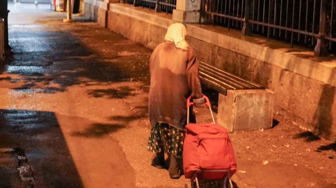 Ηλικιωμένη σέρνει το καρότσι της σε δρόμο 