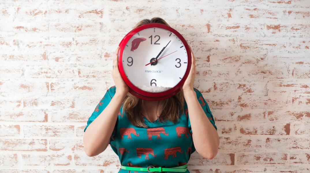 Κοπέλα κρατά στο ύψος του κεφαλιού της ένα κόκκινο ρολόι