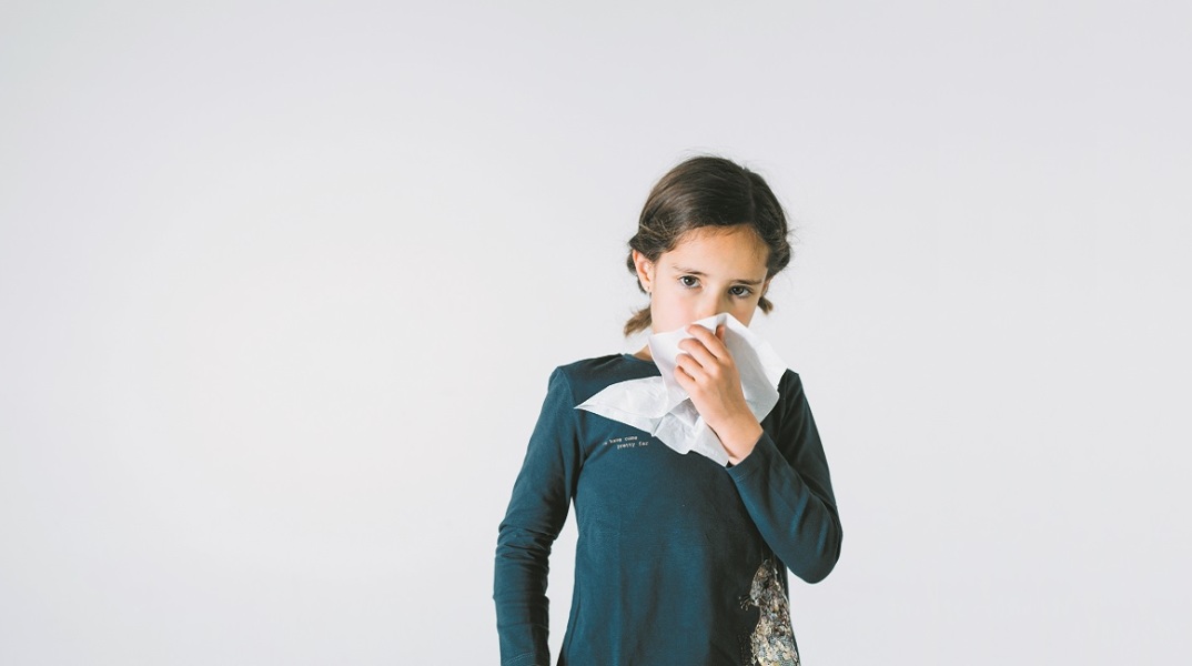 Ένα παιδί κρατάει ένα χαρτομάντηλο και κοιτάει την κάμερα. 