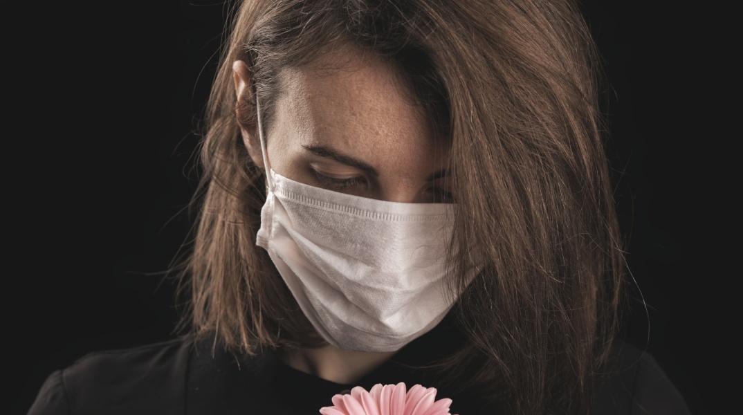 Γυναικά με μάσκα κρατά στα χέρια της ένα λουλούδι