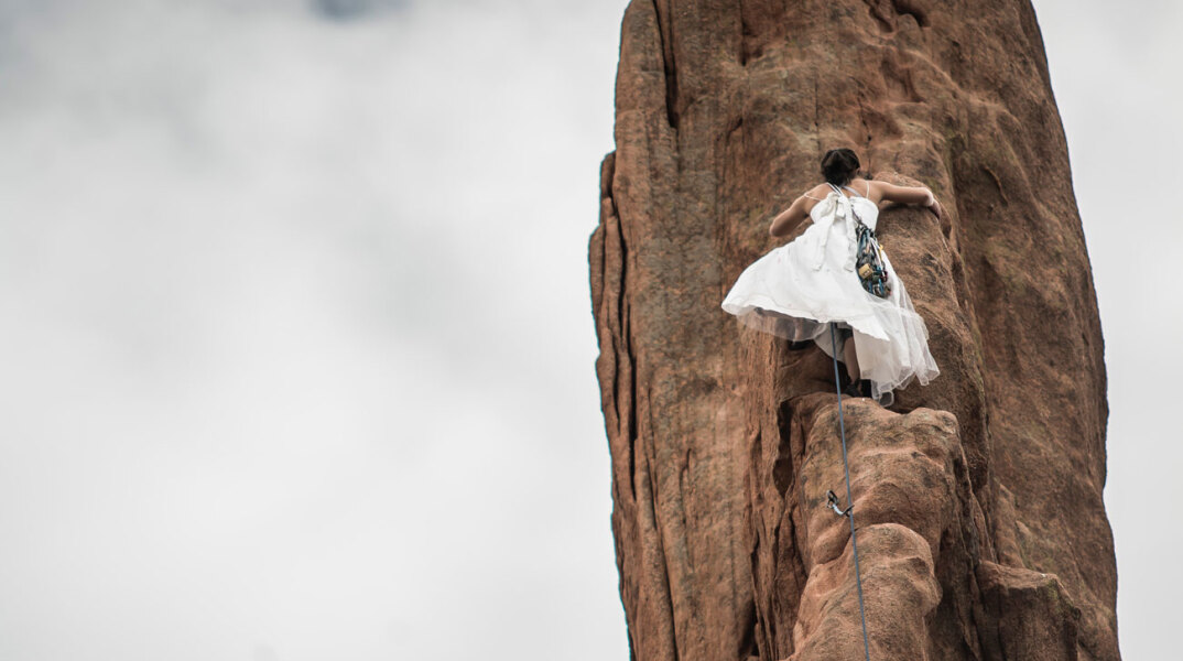 Γυναίκα με λευκό φόρεμα σκαρφαλώνει σε κάθετο βράχο