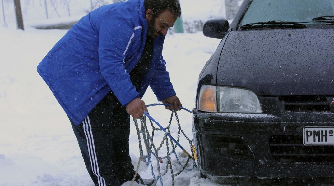 Οδηγός τοποθετεί αντιολισθητικές αλυσίδες στο όχημά του
