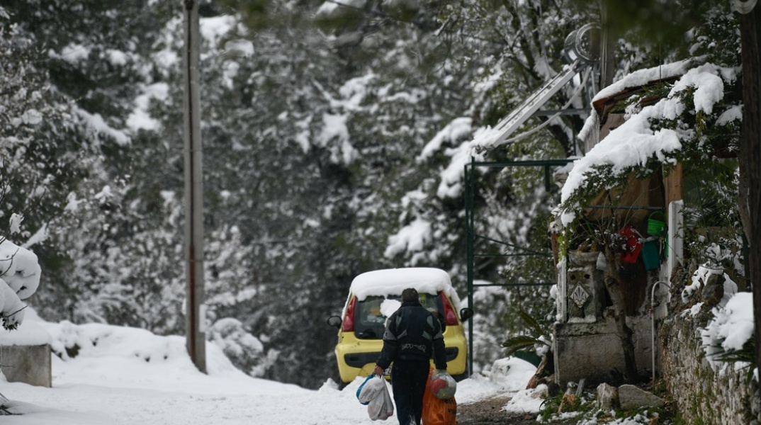 Κακοκαιρία «Φίλιππος»: Πολίτης περπατά σε δρόμο με χιόνια κουβαλώντας ψώνια