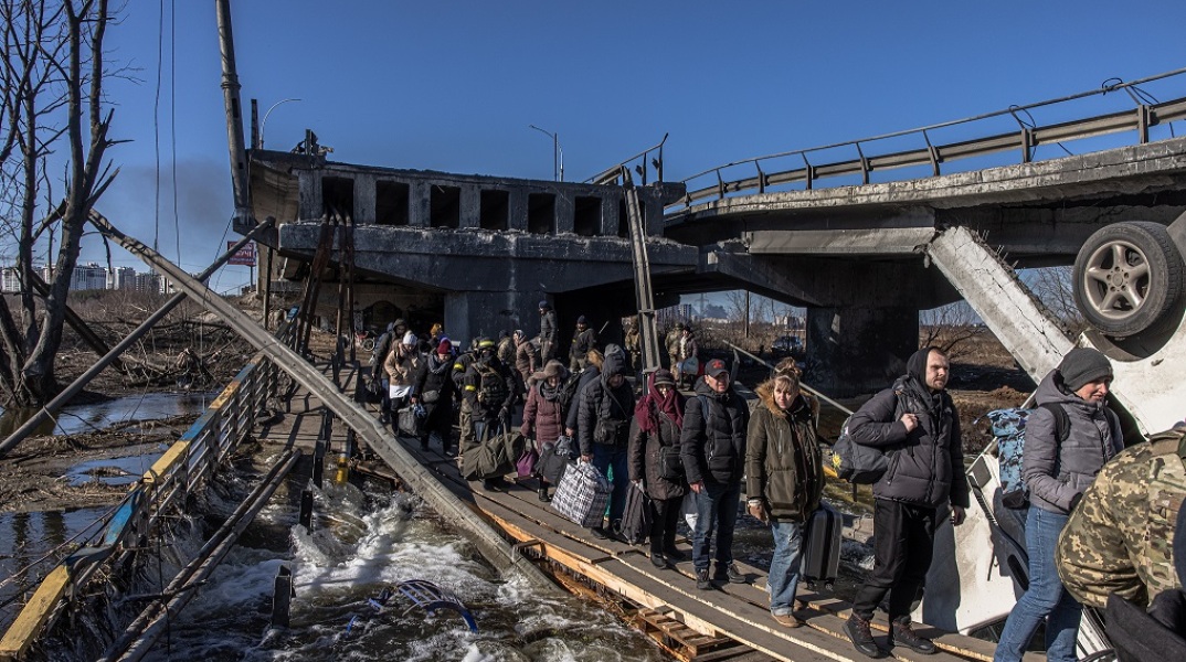 Πρόσφυγες στην Ουκρανία προσπαθούν να διασχίσουν δρόμο κάτω από βομβαρδισμένη γέφυρα