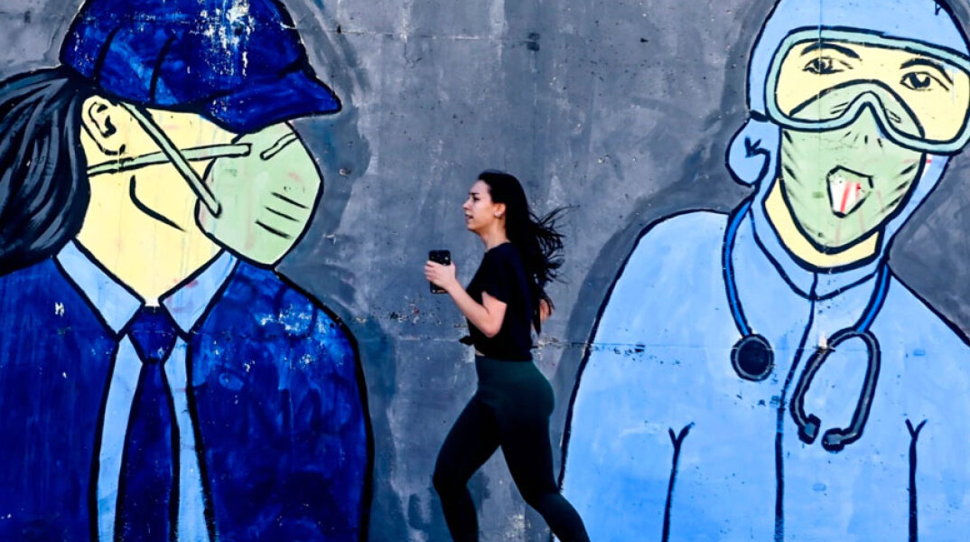 Κοπέλα κάνει τζόκινγκ, περνώντας μπροστά από mural για τον κορωνοϊό