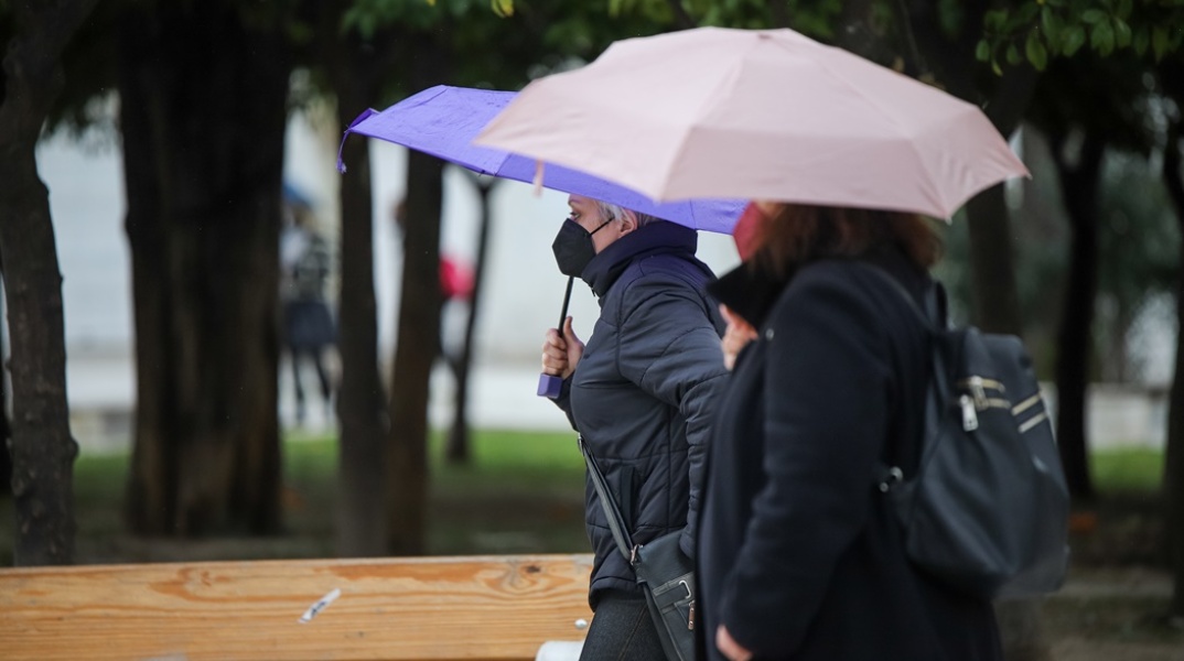 Γυναίκες περπατούν στο κέντρο της Αθήνας κρατώντας ομπρέλες