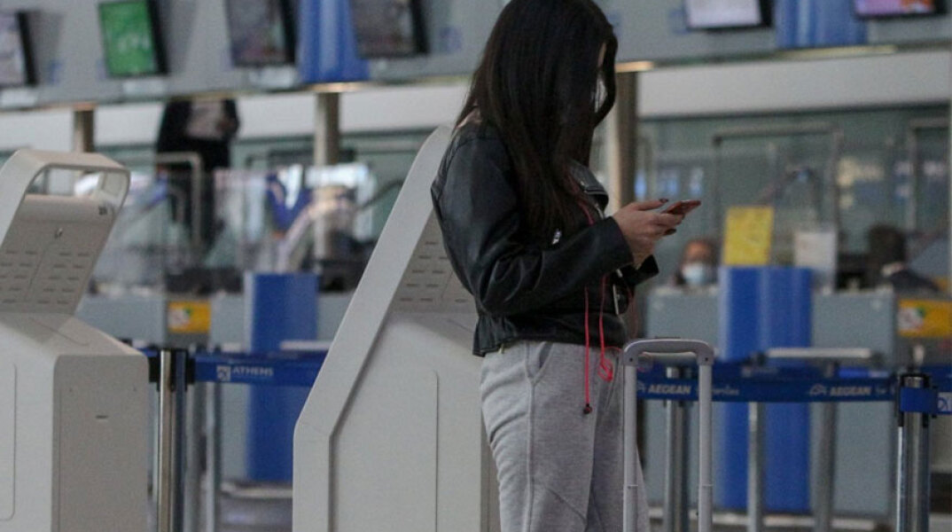 Κοπέλα στο αεροδρόμιο «Ελευθέριος Βενιζέλος» κοιτά το κινητό της τηλέφωνο