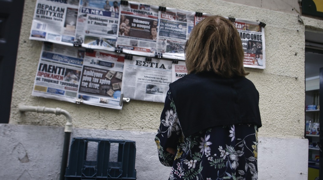 Γυναίκα διαβάζει τα πρωτοσέλιδα των εφημερίδων που βρίσκονται αναρτημένα σε περίπτερο